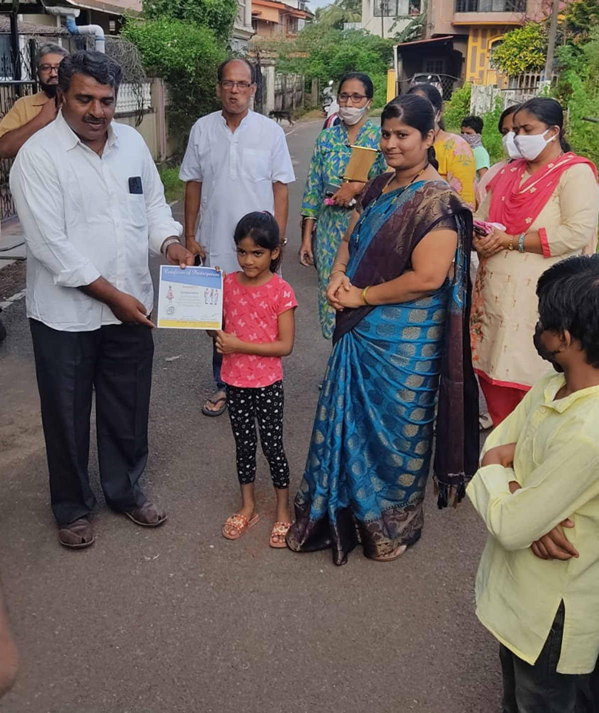 Award of participation certificate to miss Samaira Jakati for participating in the Fancy dress competition held on 15-Aug-2021. <a href=https://youtu.be/j_FD4Nt_gWg target=_blank class=blue>Competition Video</a><br><br>Seen in the photo (from left): Shri Monesh Meti presenting certificate to Samaira Jakati, Professor Shri Viraj Govind Mahatme (background), Association President Shri Santosh Desai, Smt Monesh Meti, Smt Shantaram Desai and Smt. Vijayshri B. Gunjikar (background)